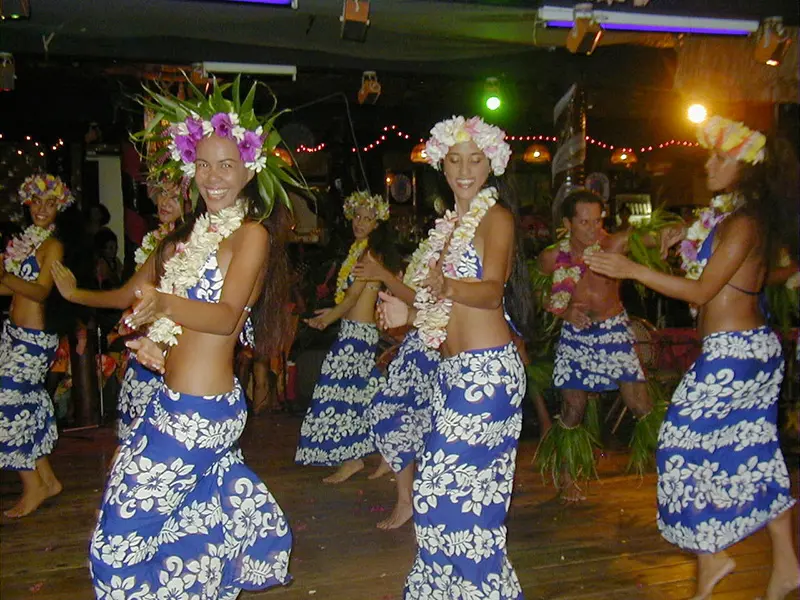 Modern hula dancers in bar in Tahiti in blue floral skirts and tops with floral head dresses