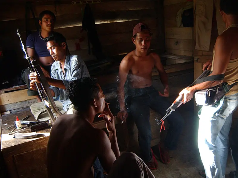Achenese rebels resting in hut smoking and holding weapons