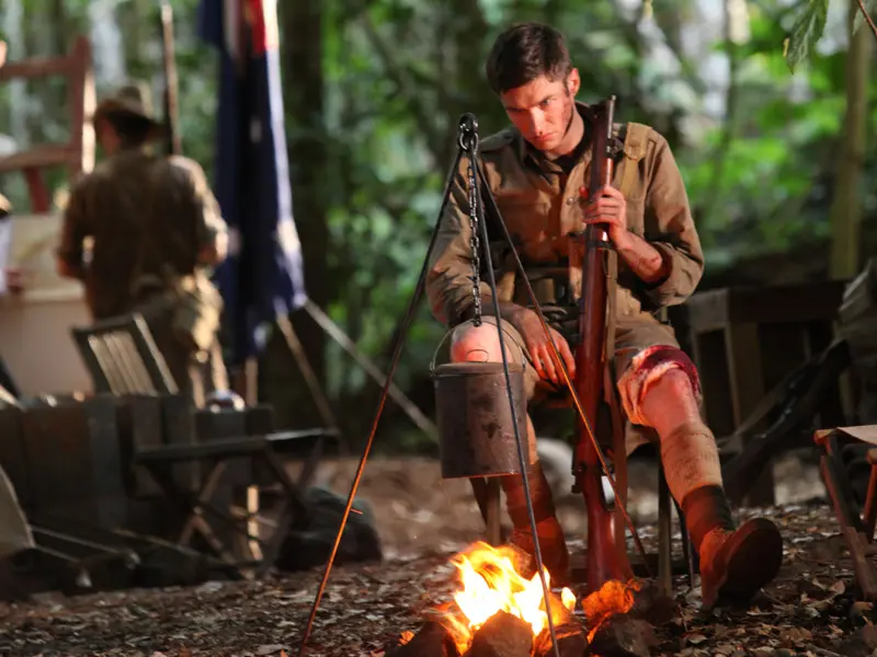 Young Australian soldier at camp in the Malaysian jungle in front of an open campfire holding rifle