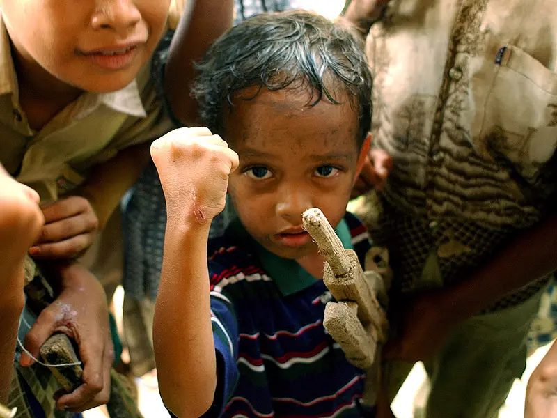 Young child with fake rifle raises fist at camera with achenes rebels