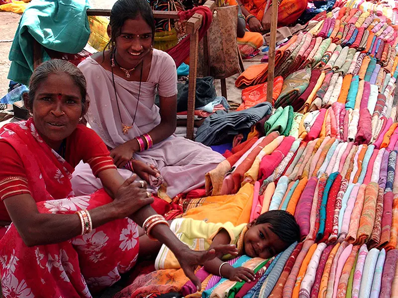 Two women sit next to and a child lays on a stack of colourful saris in India