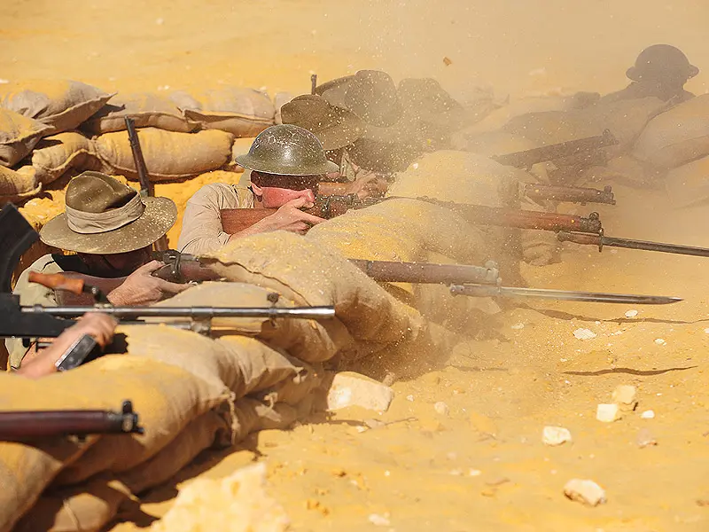 a group of soldiers with bayonet rifles fire from behind sandbags