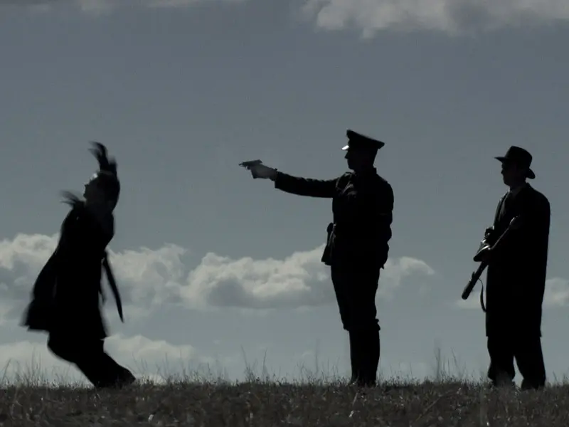Silhouette of gestapo officer shooting prisoner in uniform in field with hand gun