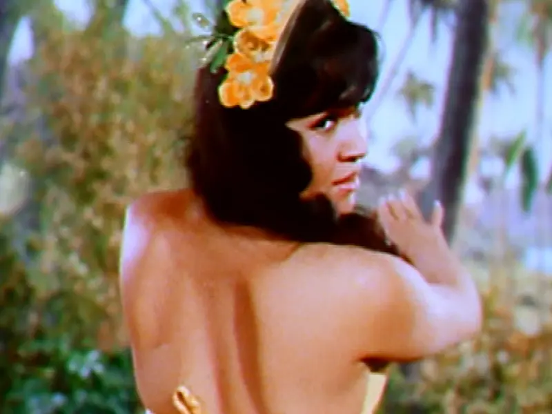 Hula dancer from 1960s Scoptione Keep Your Eyes on the Hands looks over her shoulder with orange flowers in her hair
