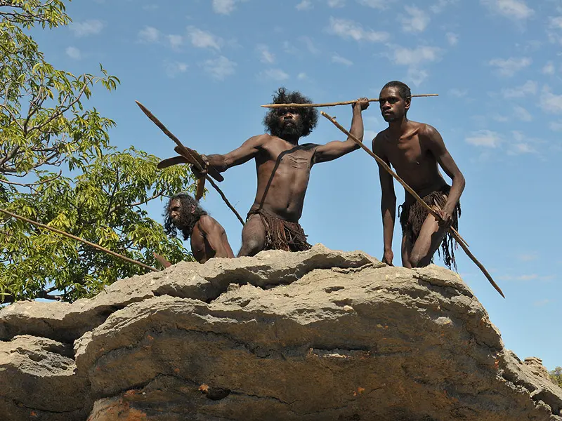 three aboriginal warriors throw spears from a rocky ledge