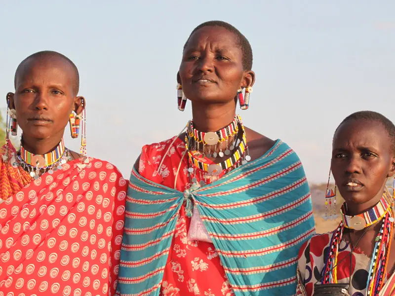 Three female Massai villagers in bright coloured clothes in East Africa